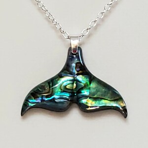 May include: A silver chain necklace with a green and blue abalone shell whale tail pendant.