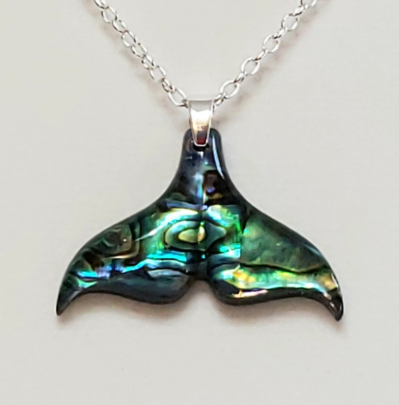 May include: A silver chain necklace with a green and blue abalone shell whale tail pendant.