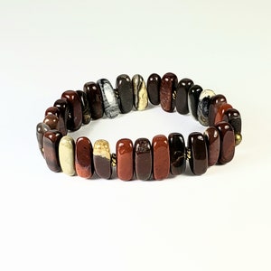 May include: A red, brown, and white stone bracelet with gold accents. The bracelet is made of rectangular stones and is strung together with gold wire.