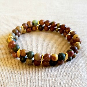 May include: A double-strand bracelet with brown, green, and gold beads. The beads are made of natural stone and are separated by gold spacers.
