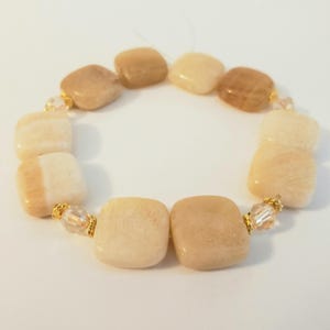 May include: A bracelet featuring square, light-colored stones in shades of beige and cream. The stones are strung together with gold-colored accents and clear beads, creating a neutral-toned accessory.