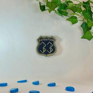 May include: A navy blue patch with gold trim and the word "EXPEDITION" arched across the top. The number "33" is in gold, stylized in the center. The patch is in the shape of a shield.