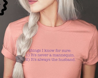 May include: A pink t-shirt with a purple text graphic that reads "things I know for sure: 1) It's never a mannequin. 2) It's always the husband."