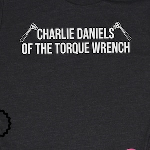 May include: A black t-shirt with white text that reads "Charlie Daniels of the Torque Wrench" with a wrench graphic on either side of the text.