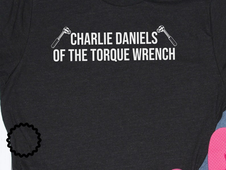 May include: A black t-shirt with white text that reads "Charlie Daniels of the Torque Wrench" with a wrench graphic on either side of the text.