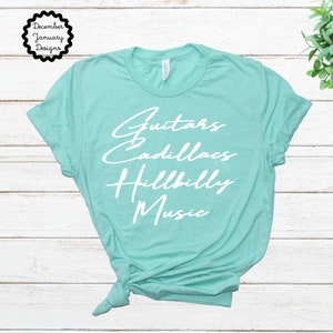 Puede incluir: Una camiseta turquesa con el texto "Guitars Cadillacs Hillbilly Music" impreso en blanco.