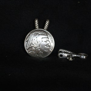 May include: Silver pendant featuring a profile of an American Indian with a feather headdress. The pendant is attached to a twisted silver chain.