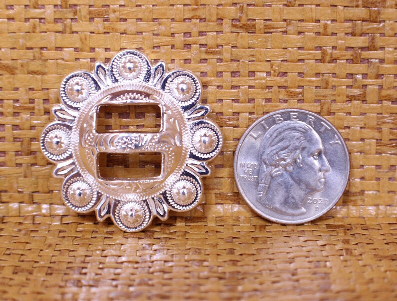 May include: Silver-toned metal buckle with a decorative design and two slots. The buckle is about the size of a US quarter.