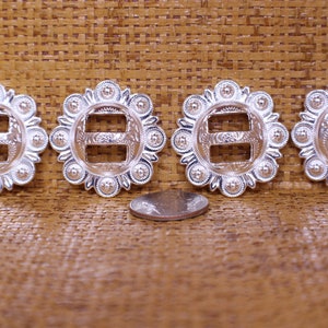 May include: Four silver-toned metal buckles with a decorative design. Each buckle has a double-slot opening and a circular design with raised dots around the edge. A US quarter is included for size reference.