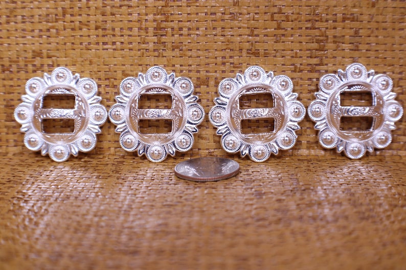 May include: Four silver-toned metal buckles with a decorative design. Each buckle has a double-slot opening and a circular design with raised dots around the edge. A US quarter is included for size reference.