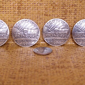 May include: Four silver-toned commemorative coins with the inscription "In God We Trust" and "Oregon Trail Memorial 1926". Each coin features a wagon train with a covered wagon and oxen.