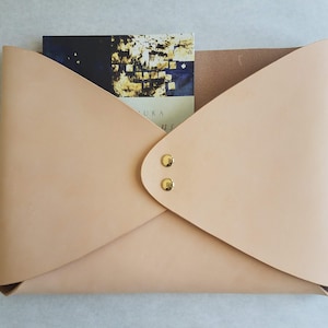 May include: A light beige leather envelope with two gold metal snaps. The envelope is folded in half and has a book inside.