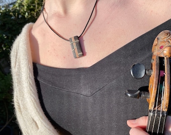 May include: A woman wearing a black top and a white cardigan is holding a violin. She is wearing a necklace with a wooden pendant.