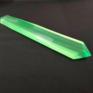 May include: A long, translucent green crystal with a pointed tip. The crystal is smooth and polished.