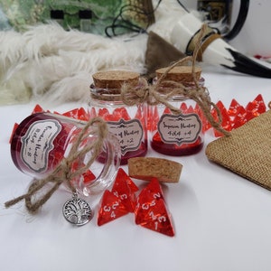 May include: Two small glass jars filled with red dice and labeled with "Greater Healing 8d4 + 8" and "Superior Healing 4d4 + 4".  There are several red dice scattered around the jars, including a few with the numbers 2 and 4 visible.