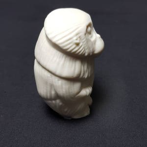 May include: A white ceramic figurine of a monkey sitting with its head tilted to the side.