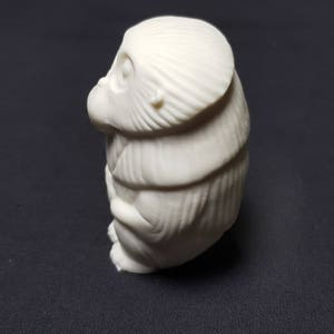 May include: A white ceramic figurine of a monkey sitting with its arms crossed. The monkey has a detailed face and fur.