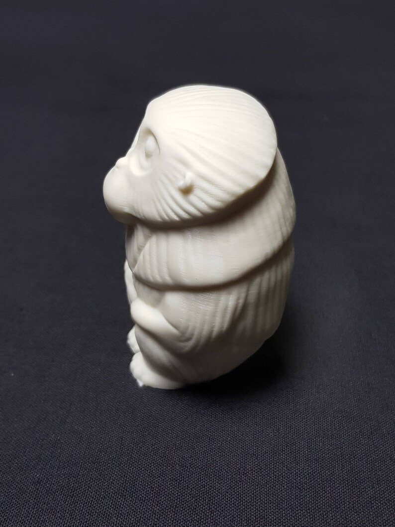 May include: A white ceramic figurine of a monkey sitting with its arms crossed. The monkey has a detailed face and fur.