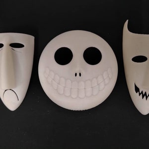 May include: Three white Halloween masks with different facial expressions. The masks are made of a smooth, white material and have black details. The first mask has a sad expression, the second mask has a wide smile, and the third mask has a sinister grin.