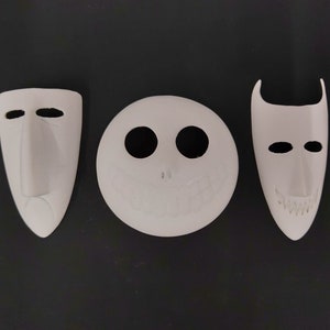 May include: Three white ceramic masks with different facial expressions. The masks are all in the shape of a human face, but each has a unique design. The first mask has a long nose and a sad expression. The second mask has a wide smile and two large eyes. The third mask has a pointed chin and a mischievous expression.