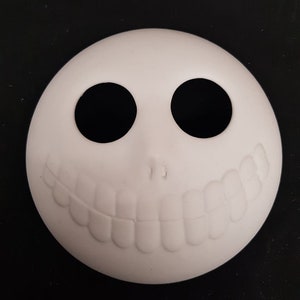 May include: White ceramic blank ornament shaped like a face with two black eye holes and a toothy grin.