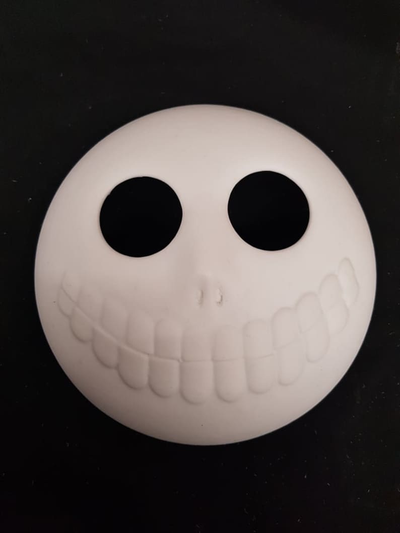 May include: White ceramic blank ornament shaped like a face with two black eye holes and a toothy grin.