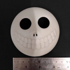 May include: White plastic mask with a black smiling face, two black eyes, and a small black nose. The mask is approximately 5 inches wide.