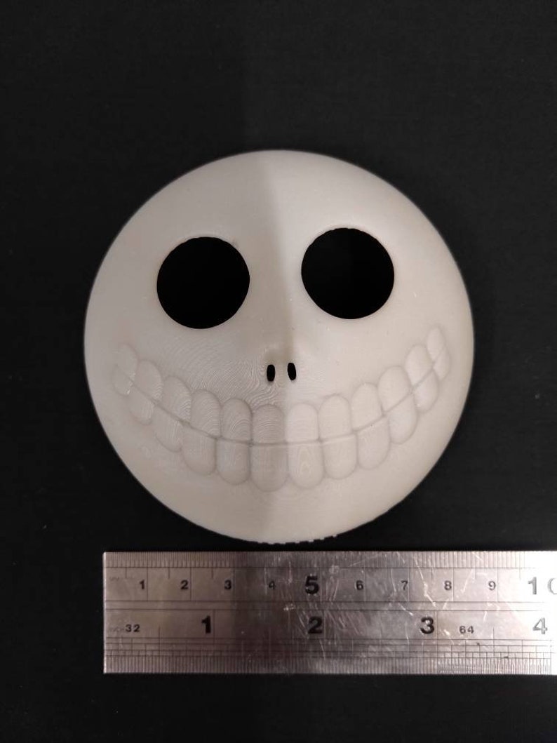 May include: White plastic mask with a black smiling face, two black eyes, and a small black nose. The mask is approximately 5 inches wide.