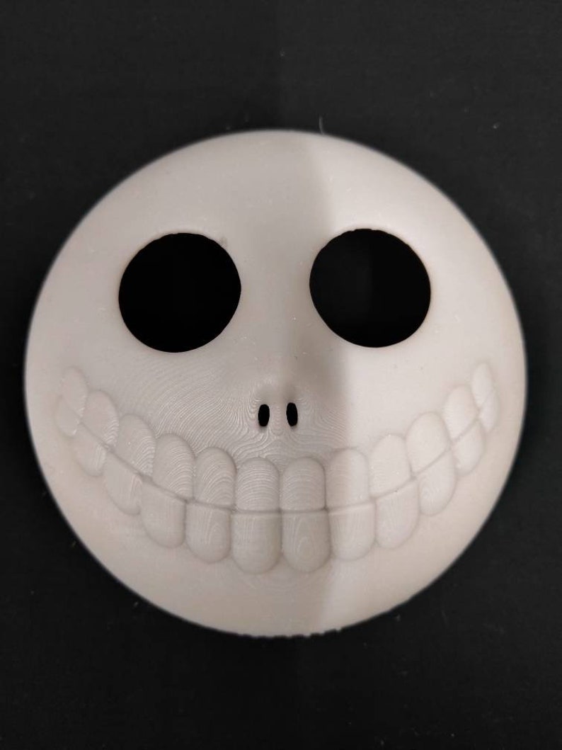 May include: A white 3D printed mask with a wide smile and two black eye holes. The mask is a popular Halloween decoration.