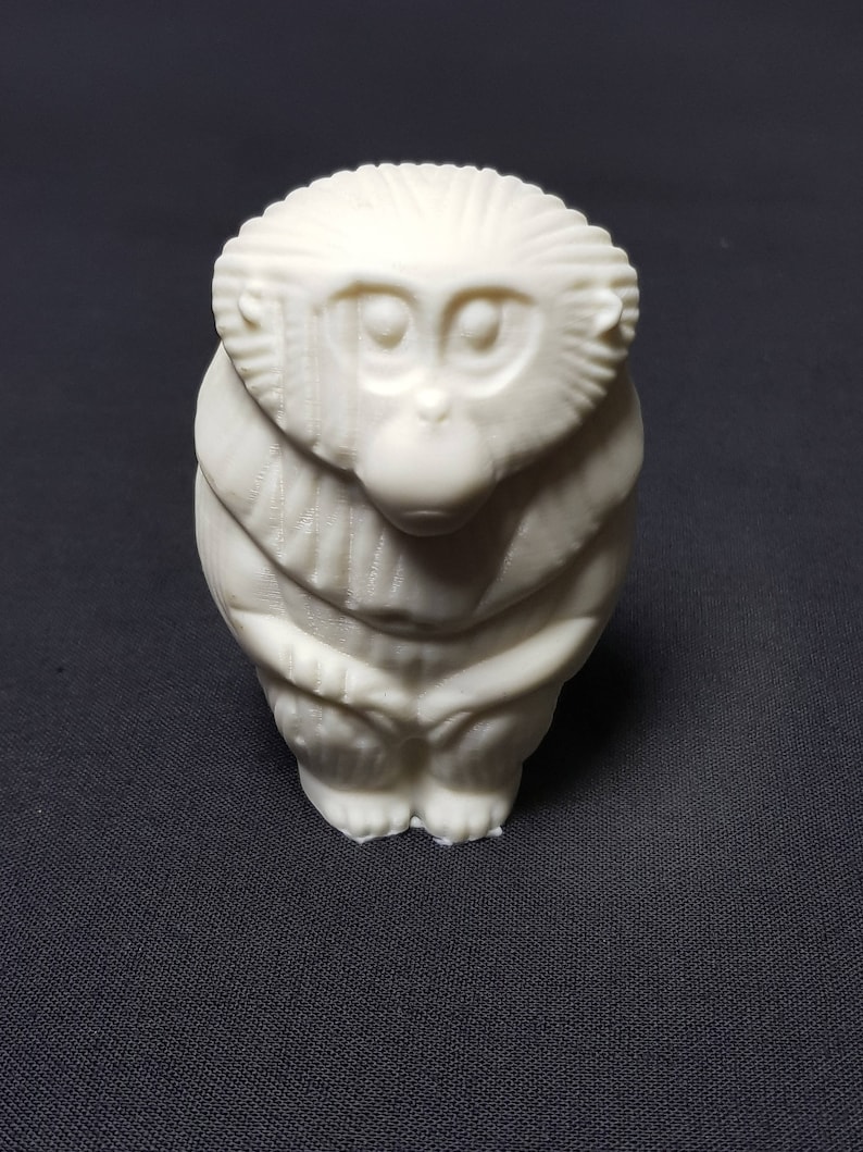 May include: A white ceramic figurine of a monkey sitting with its hands clasped in front of it. The monkey has a detailed face with large eyes and a small nose.
