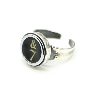 Può includere: Un anello d'argento con un tasto di macchina da scrivere nero e bianco con il simbolo ampersand e il numero 7 in oro.