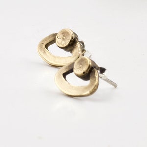 Op de afbeelding: Een paar gouden oorbellen met een uniek, abstract ontwerp. Elke oorbel heeft een ronde vorm met een kleinere cirkel die uit het midden is geknipt, waardoor een ring-achtig effect ontstaat.
