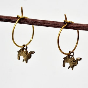 Puede incluir: Un par de pendientes de aro dorados con un pequeño dije de camello colgando de cada aro.