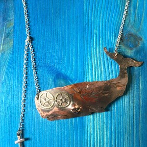 May include: A copper whale pendant necklace with two brass gears for eyes. The necklace is on a silver chain with an anchor charm.