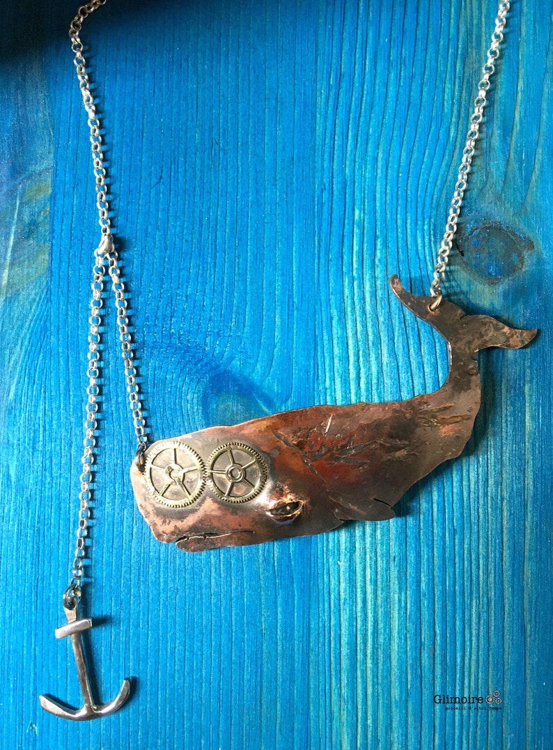 May include: A copper whale pendant necklace with two brass gears for eyes. The necklace is on a silver chain with an anchor charm.