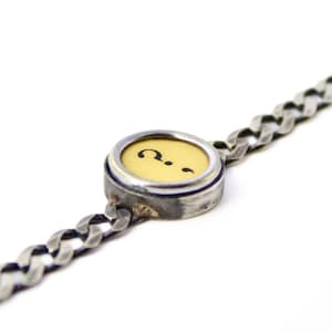 Könnte beinhalten: Ein silbernes Kettenarmband mit einem runden Anhänger, der eine vintage Schreibmaschinentaste mit einem Fragezeichen und einem Semikolon zeigt.