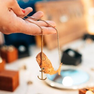 May include: A gold chain necklace with a whale pendant and an anchor charm. The whale is detailed with a textured surface.