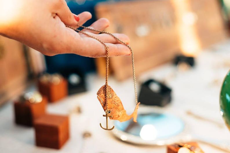 May include: A gold chain necklace with a whale pendant and an anchor charm. The whale is detailed with a textured surface.
