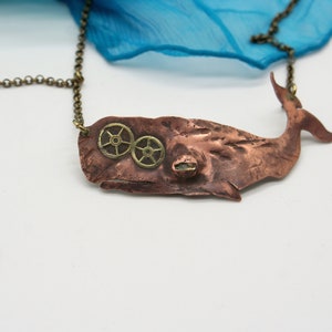 May include: A copper whale pendant necklace with brass gears and an anchor charm. The whale is textured and has a steampunk aesthetic.