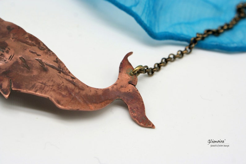 May include: A copper whale tail pendant necklace with a brass chain. The whale tail is textured and has a rustic look. The chain is attached to the top of the tail.