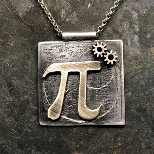 May include: A silver necklace with a square pendant featuring the mathematical symbol pi in gold, with two small gold gears on the top right corner.