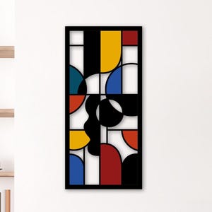 Puede incluir: Una obra de arte mural rectangular negra con un diseño geométrico. La obra presenta formas en rojo, amarillo, azul, negro y blanco. La pieza está montada en una pared blanca y tiene un marco negro. Diseño abstracto moderno.