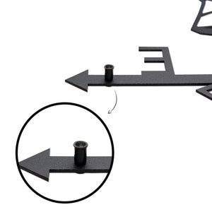 May include: Close-up of a black metal wind vane with an arrow pointing to the right. The arrow is attached to a metal rod with a small metal pin. The pin is used to adjust the direction of the arrow.