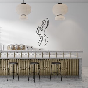 May include: A white marble bar counter with a gold metal divider and three black metal bar stools. A black metal line art sculpture of a person is on the wall behind the bar counter.