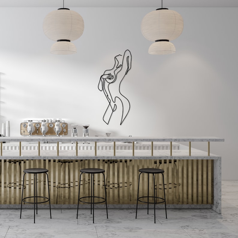 May include: A white marble bar counter with a gold metal divider and three black metal bar stools. A black metal line art sculpture of a person is on the wall behind the bar counter.