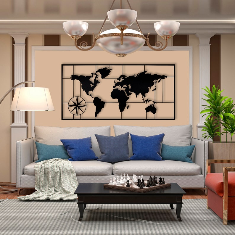 May include: A black metal world map wall decor with a compass design, hanging above a white sofa with blue pillows and a chessboard on a coffee table.