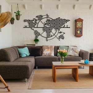 May include: A brown sectional sofa with pillows sits in front of a black metal world map wall decor with a compass design. The room has white brick walls, a wooden floor, and a wooden coffee table with a vase of pink roses.