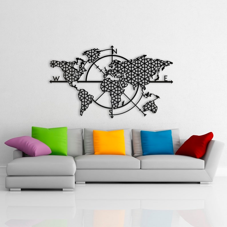 May include: A black metal world map wall decor with a compass design. The map is made of intricate geometric patterns and features the continents of North America, South America, Europe, Asia, Africa, and Australia. The compass points north, south, east, and west. The map is hanging on a white wall above a gray sectional sofa with colorful throw pillows.