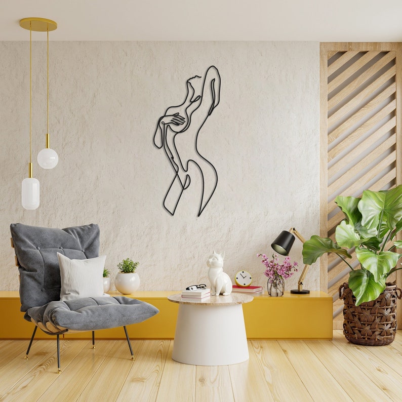 May include: A black metal wall sculpture of a stylized female figure in a minimalist line art style. The sculpture is mounted on a white wall in a modern living room setting.