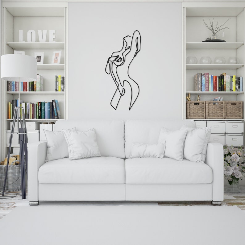 May include: A white sofa with two pillows in a living room setting. A black metal line art sculpture of a person is on the wall behind the sofa. The word "LOVE" is on a white shelf above the sofa.
